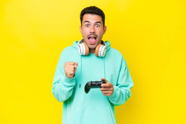 Bir video oyunu kontrolörüyle oynayan yakışıklı genç adam izole duvarın üzerinde galibiyeti kutluyor.