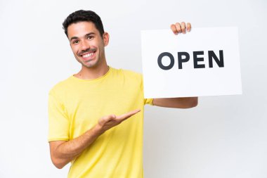 İzole edilmiş beyaz arka planda genç yakışıklı bir adam elinde açık yazılı bir pankart tutuyor ve onu işaret ediyor.