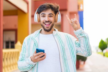 Yakışıklı bir Arap açık havada gezici bir hareketle müzik dinliyor.