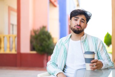 Yakışıklı bir Arap, üzgün bir ifadeyle açık havada kahvesini yudumluyor.