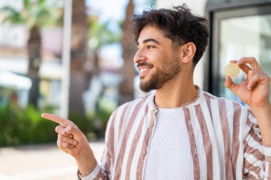 Dışarıda Bitcoin tutan yakışıklı bir Arap, bir ürünü sunmak için yan tarafı işaret ediyor.