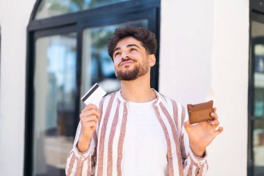 Açık havada cüzdan ve kredi kartı tutan yakışıklı bir Arap.