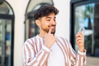 Dışarıdaki yakışıklı Arap adam mutlu bir ifadeyle görünmez diş telleri tutuyor.