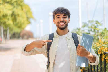 Genç bir Arap öğrenci açık havada ve onu işaret ediyor.