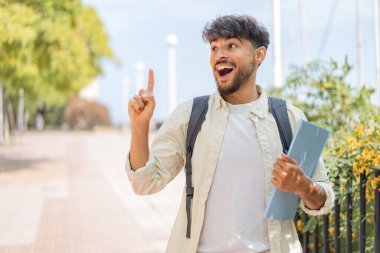 Açık havada genç bir Arap öğrenci parmağını kaldırarak çözümü anlamaya çalışıyor.