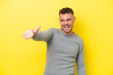Sarı arka planda izole edilmiş beyaz, yakışıklı genç bir adam baş parmak işareti yapıyor.