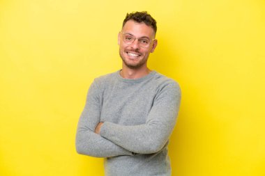 Sarı arka planda izole edilmiş, kolları çapraz ve ileriye bakan beyaz, yakışıklı genç bir adam.