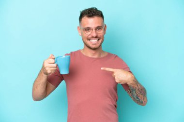 Kafkasyalı genç bir adam elinde kahve fincanı tutarken mavi arka planda şaşırmış bir yüz ifadesi var.
