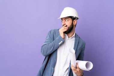 Miğferli genç bir mimar. Mor arka plan üzerinde planlar tutuyor. Yan tarafa bakarken sürpriz jest yapıyor.