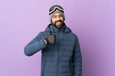 İzole edilmiş mor arka planda snowboard gözlüklü kayakçı iyi niyet gösterisi yapıyor.