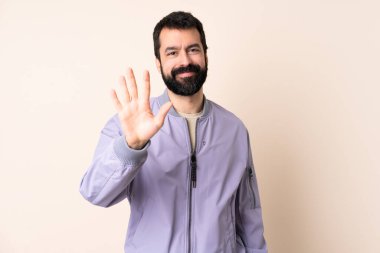 Sakallı, ceketli, soyutlanmış bir beyaz adam. Parmaklarıyla beşi sayıyor.