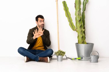 Bahçıvan içeride yerde oturuyor. Gergin bir şekilde ellerini öne uzatıyor.