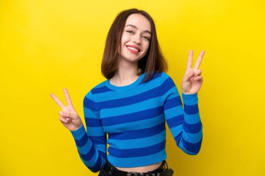 Sarı arka planda izole edilmiş genç Ukraynalı kadın iki eliyle zafer işareti gösteriyor.