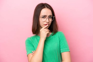 Genç Ukraynalı bir kadın pembe arka planda gözlüklü ve kuşkuları olan