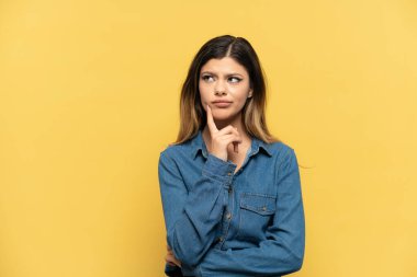 Young Russian girl isolated on yellow background having doubts and thinking