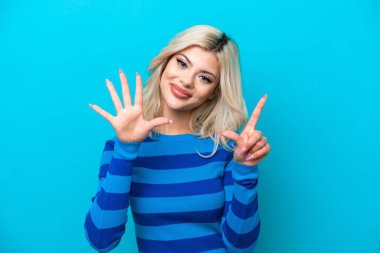 Mavi arka planda izole edilmiş genç Rus kadın parmaklarıyla yediyi sayıyor