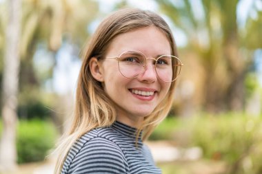 Açık havada gözlüklü, neşeli bir yüzü olan genç sarışın kadın.