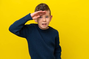 Küçük beyaz çocuk sarı arka planda izole edilmiş. Bir şeye bakmak için uzaklara bakıyor.