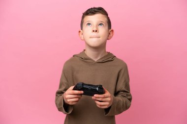 Pembe arka planda izole edilmiş bir bilgisayar oyunu kontrolörüyle oynayan beyaz bir çocuk.