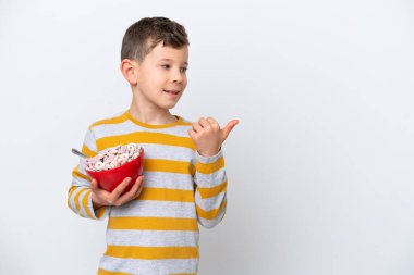 Beyaz arka planda yalıtılmış mısır gevreği kasesi tutan küçük beyaz çocuk bir ürün sunmak için yan tarafı işaret ediyor.