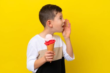 Sarı arka planda izole edilmiş kornet dondurması olan beyaz bir çocuk ağzı sonuna kadar açık bağırıyor.