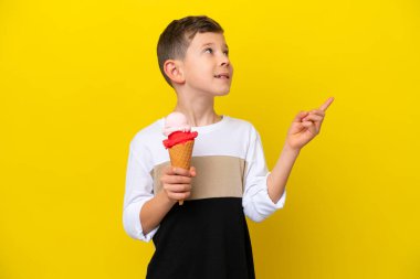 Sarı arka planda izole edilmiş kornet dondurması olan beyaz çocuk harika bir fikre işaret ediyor.