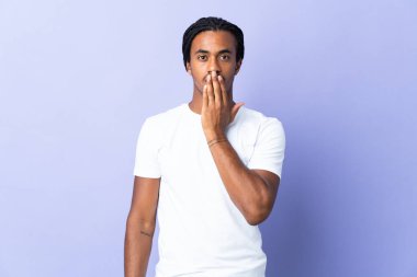 Örgülü genç Afrikalı Amerikalı adam, mor arka planda izole edilmiş, ağzı elle kapatılmış.