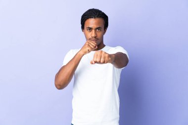 Örgülü genç Afrikalı Amerikalı adam mor arka planda izole edilmiş dövüşçü jesti ile