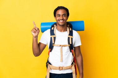 Sarı arka planda büyük bir sırt çantası olan genç dağcı harika bir fikre işaret ediyor.