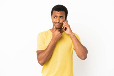 Afrikalı yakışıklı adam cep telefonunu izole edilmiş beyaz arka plan üzerinde kullanıyor. Şüpheleri ve düşünceleri var.