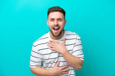 Kafkasyalı genç adam mavi arka planda izole edilmiş, çok gülümsüyor.