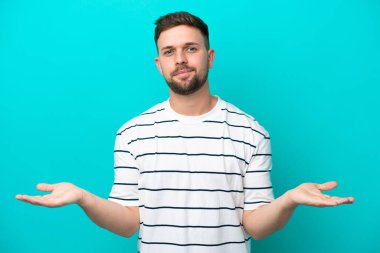 Kafkasyalı genç adam mavi arka planda izole edilmiş. Şüpheleri var.