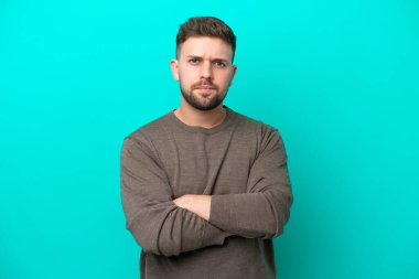 Mavi arka planda izole edilmiş genç beyaz bir adam üzgün hissediyor.