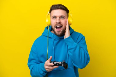 Sarı arka planda izole edilmiş, şaşırmış ve şok olmuş bir yüz ifadesiyle video oyunu kontrolörüyle oynayan genç beyaz bir adam.