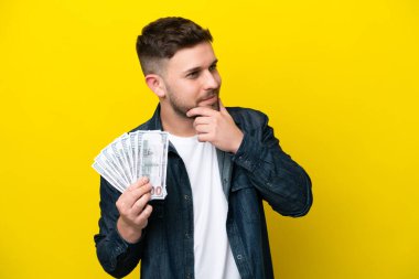 Kafkasyalı genç adam, sarı arka planda izole edilmiş bir şekilde bir sürü para alıyor. Yana bakıyor ve gülümsüyor.