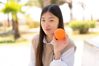 Açık havada elinde portakal tutan güzel bir Çinli kadın.