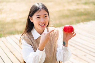 Dışarıda elmalı genç bir Çinli kadın var ve onu işaret ediyor.