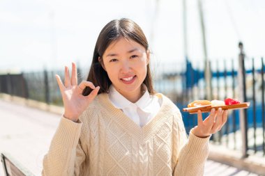 Genç Çinli bir kadın açık havada sashimi tutuyor. Parmaklarıyla 