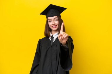 Genç üniversite mezunu Ukraynalı bir kadın sarı arka planda izole edilmiş ve parmağını kaldırıyor.