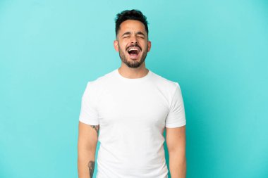 Kafkasyalı genç adam mavi arka planda izole edilmiş ve ağzı açık bağırıyor.
