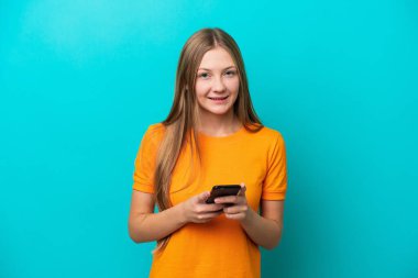 Mavi arka planda izole edilmiş genç bir Rus kadın cep telefonuyla mesaj gönderiyor.