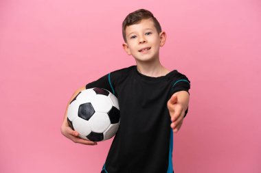 Küçük beyaz futbolcu çocuk pembe arka planda izole edilmiş iyi bir anlaşma için el sıkışıyor.
