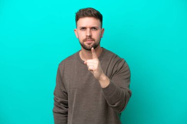 Mavi arka planda izole edilmiş genç beyaz adam hayal kırıklığına uğramış ve ön tarafı işaret ediyor.