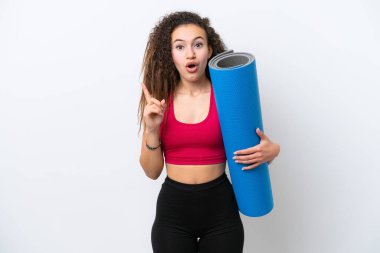 Genç Arap spor kadını yoga derslerine giderken beyaz arka planda izole edilmiş bir minder tutuyor. Çözümün farkına varmak için parmağını kaldırıyor.