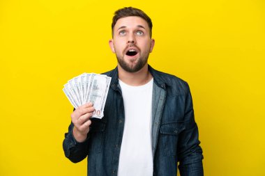 Kafkasyalı genç bir adam, sarı arka planda izole edilmiş bir şekilde bir sürü para alıyor.