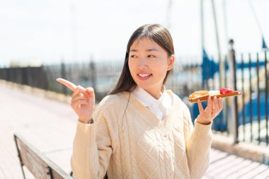 Sashimi 'yi açık havada tutan genç Çinli kadın bir ürün sunmak için kenarı işaret ediyor.