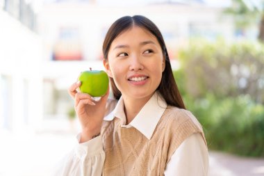Dışarıdaki güzel Çinli kadın elinde mutlu bir ifadeyle bir elma tutuyor.