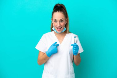 Dişçi beyaz kadın mavi arka planda şaşırtıcı bir yüz ifadesi ile izole araçlar tutuyor.