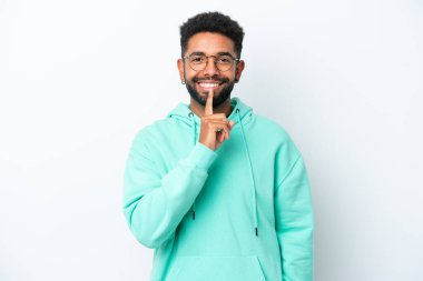 Beyaz arka planda izole edilmiş genç Brezilyalı bir adam sessizlik işareti gösteriyor. Parmağını ağzına sokuyor.