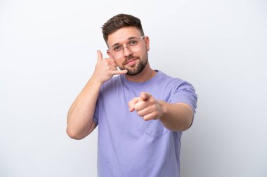 Beyaz arka planda izole edilmiş genç beyaz bir adam telefon jesti yapıyor ve ön tarafı işaret ediyor.